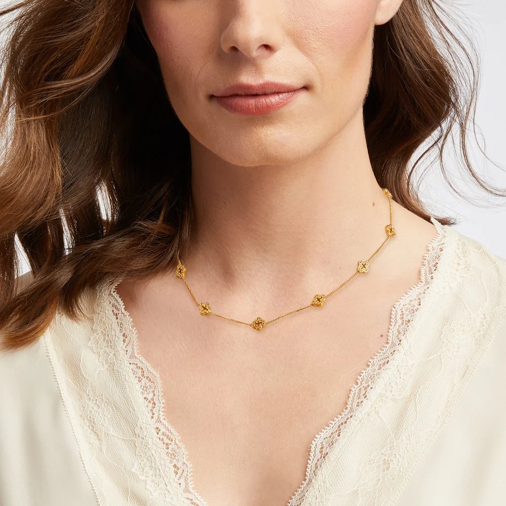 Close-up of a woman wearing a delicate gold charm necklace and a cream lace-trimmed top.