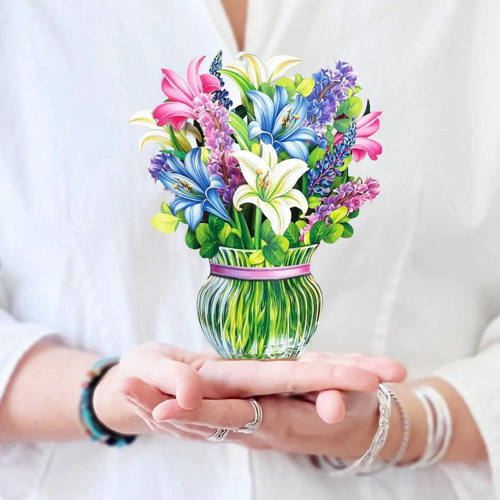 Hands hold a colorful paper flower bouquet in a green vase.