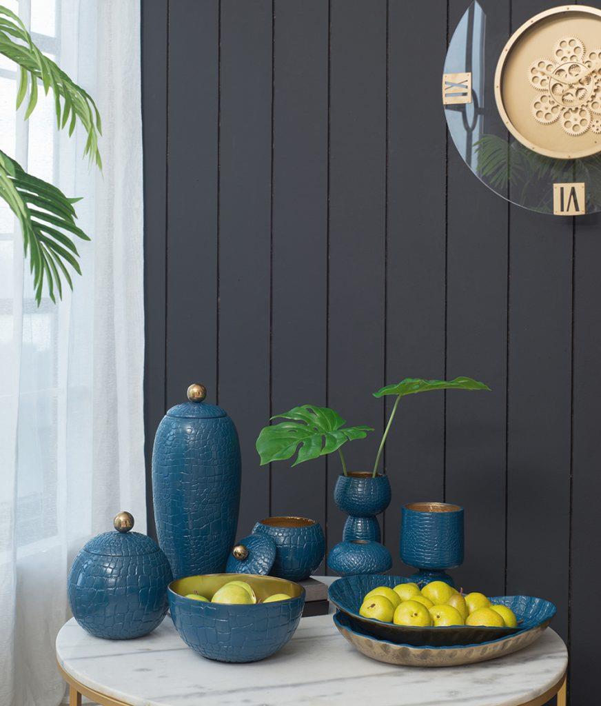 Blue ceramic decor and apples on a table with green plant accents.