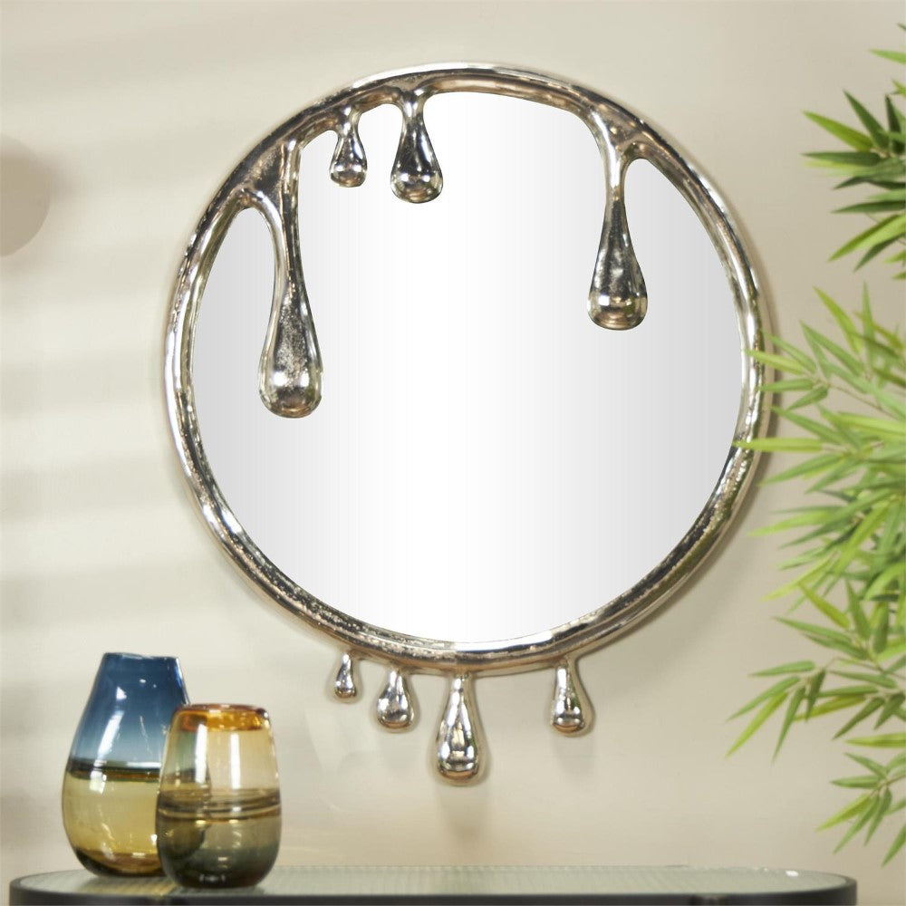Round mirror with metallic droplet design, flanked by decor and greenery.