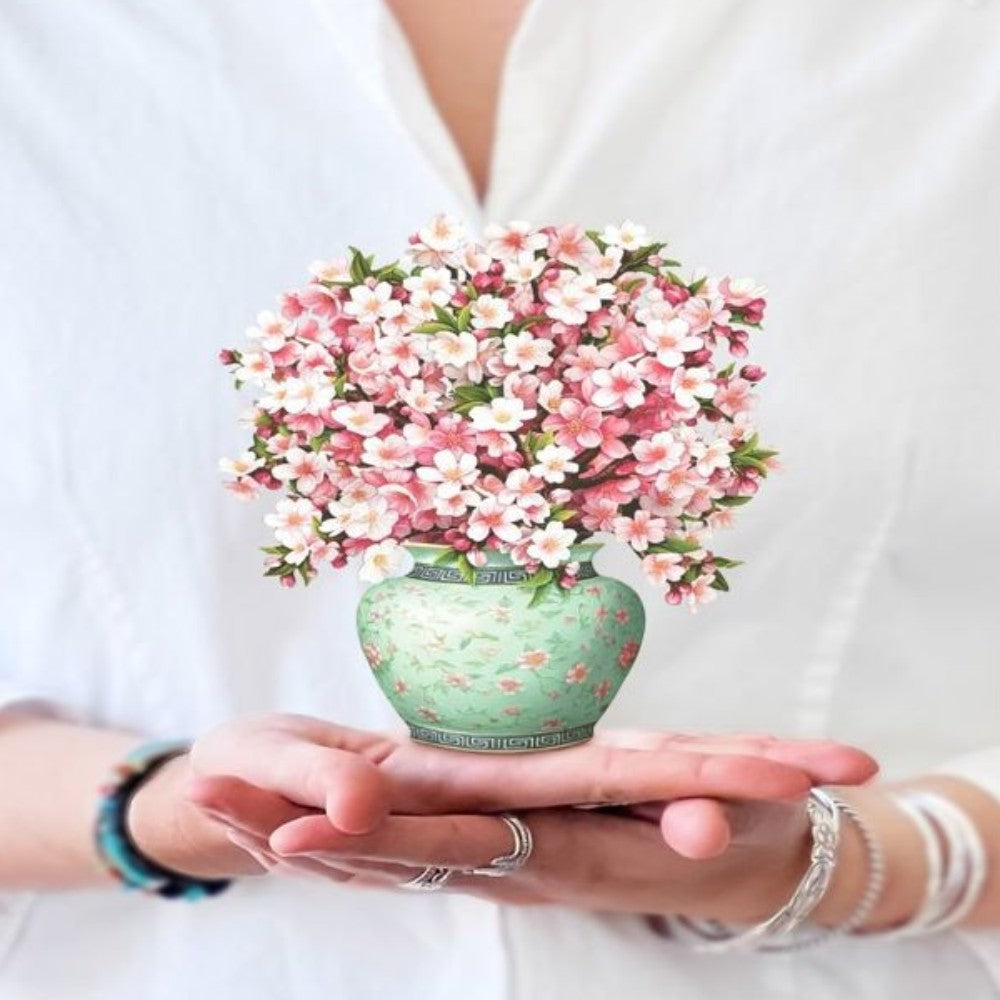 Hands hold a small vase of pink flowers.