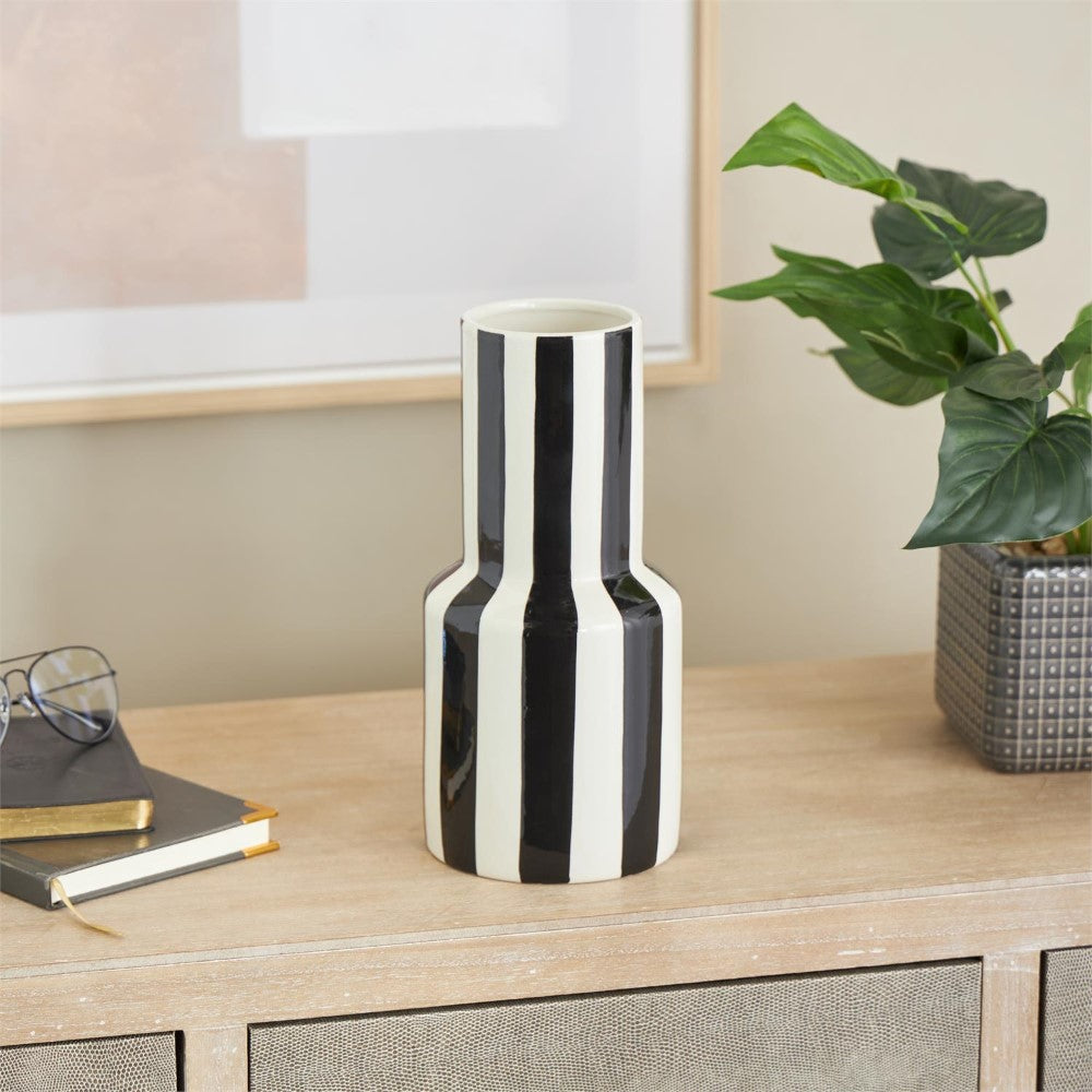 Striped vase on wooden table with plants and books nearby.