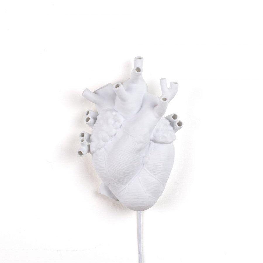 White heart-shaped sculpture with multiple tubes on a plain background.