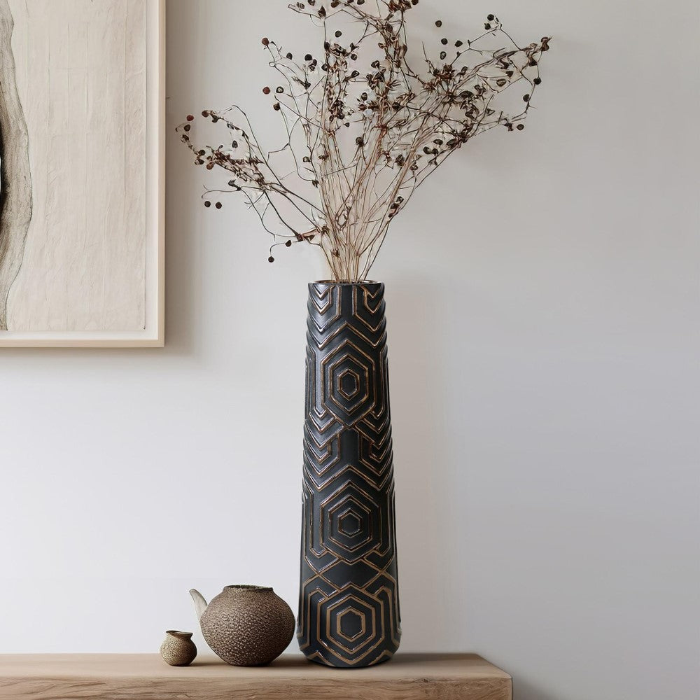 Tall patterned vase with dried branches, next to a small jug on a wooden surface.