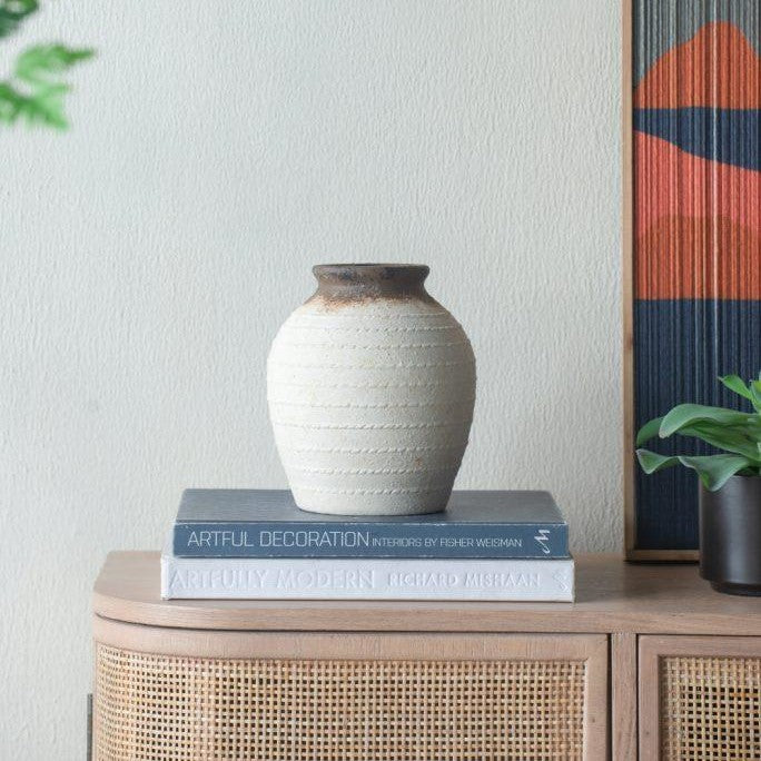 Ceramic vase on stacked books next to a plant.