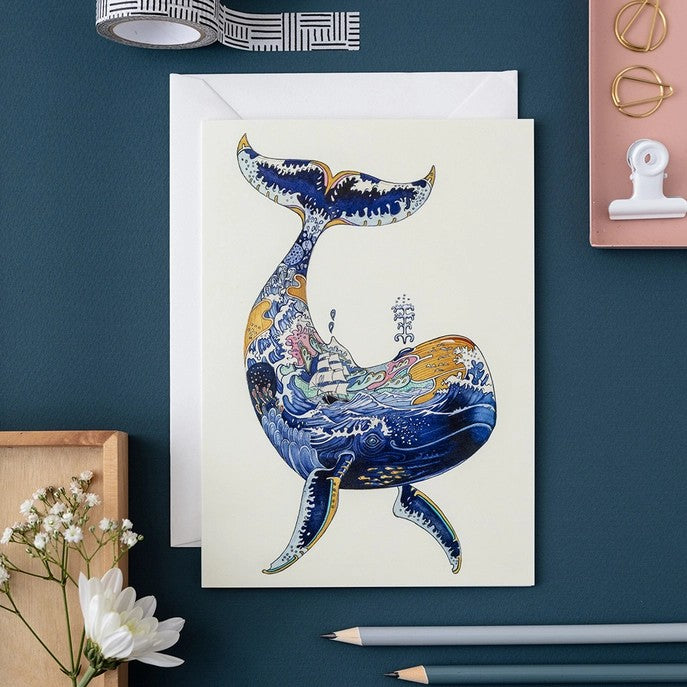 Artistic whale card with ocean scene, surrounded by stationery.