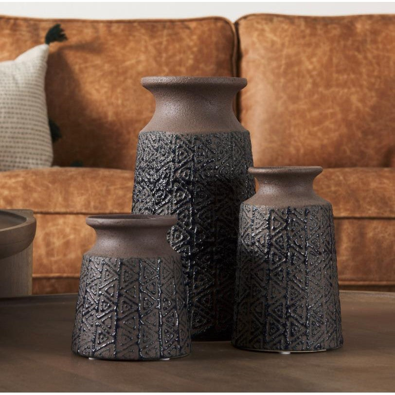 Textured vases set on a table with a brown couch in the background.