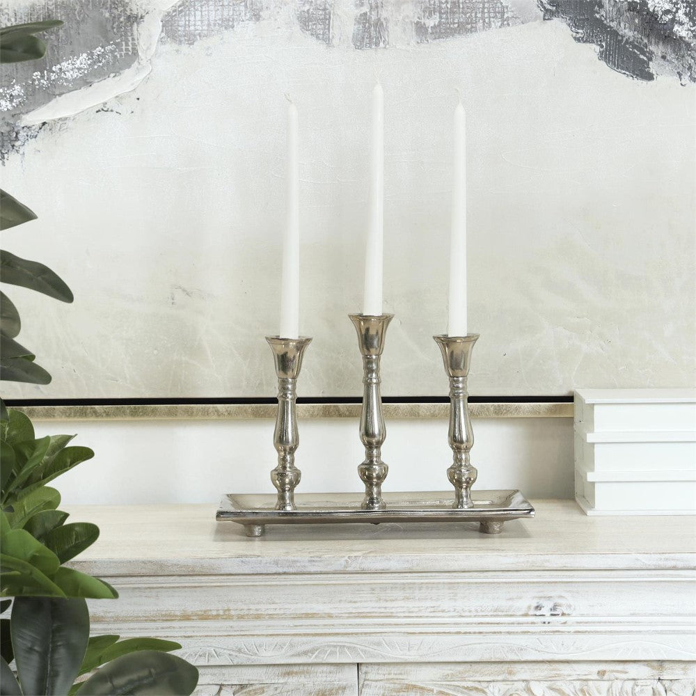 Silver candleholder with three tall candles on a white surface.