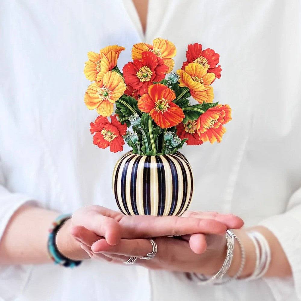 Person holding a small vase with vibrant orange and yellow flowers.