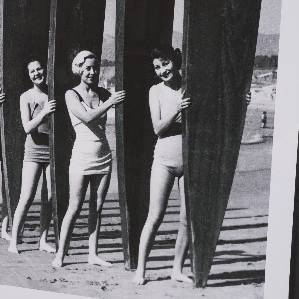 Women in swimsuits holding surfboards on a beach, vintage style.