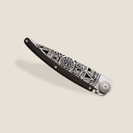 Intricately designed black and silver folding knife on a beige background.
