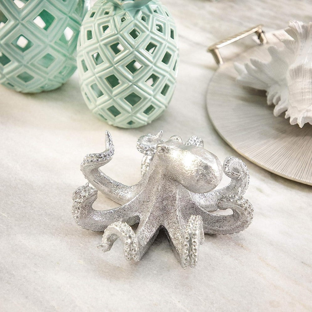 Silver octopus sculpture with decorative teal pineapples and a shell on marble surface.