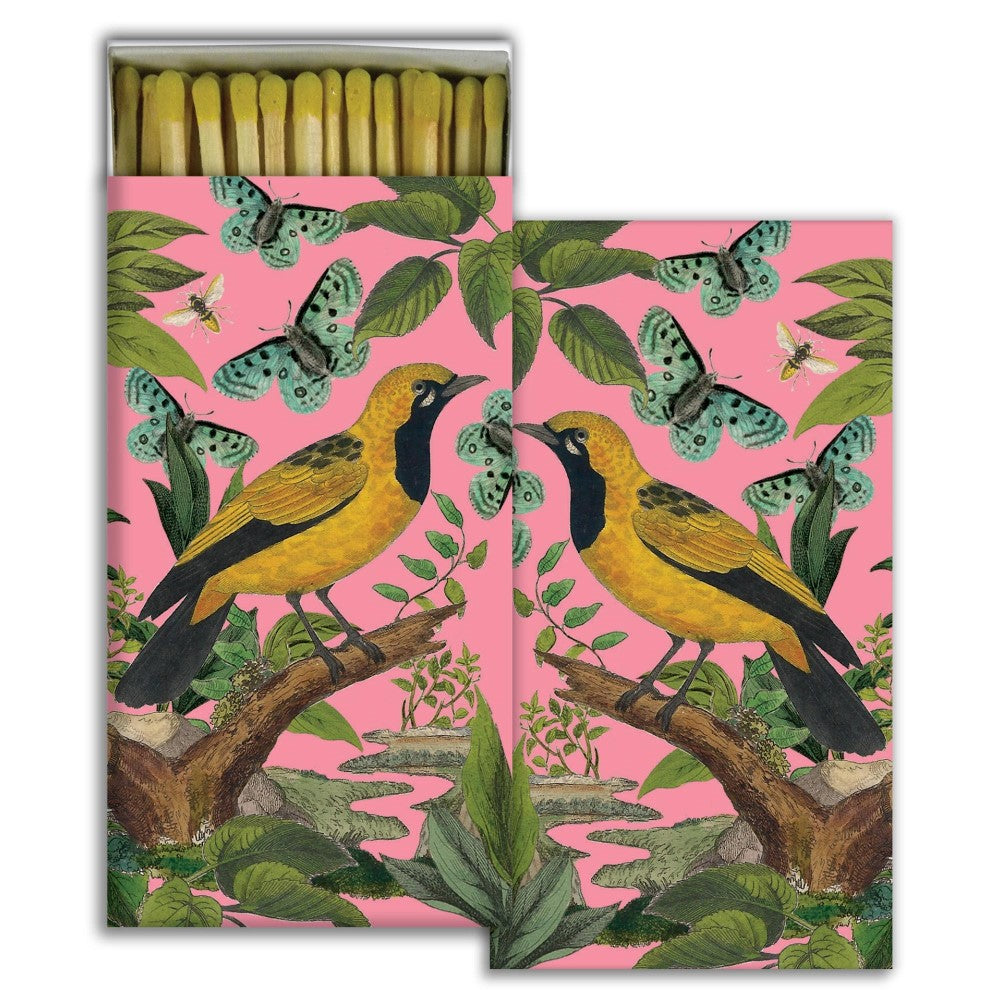 Colorful matchbox with birds, butterflies, and foliage on a pink background.