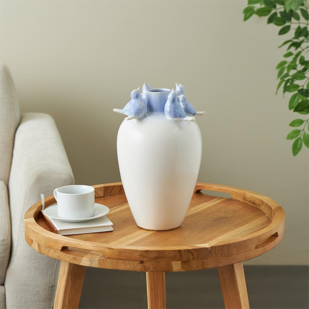 White vase with blue bird figures on a wooden table near a couch.