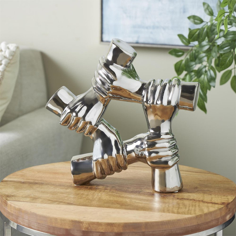 Metallic sculpture of interlocking hands on a wooden table.