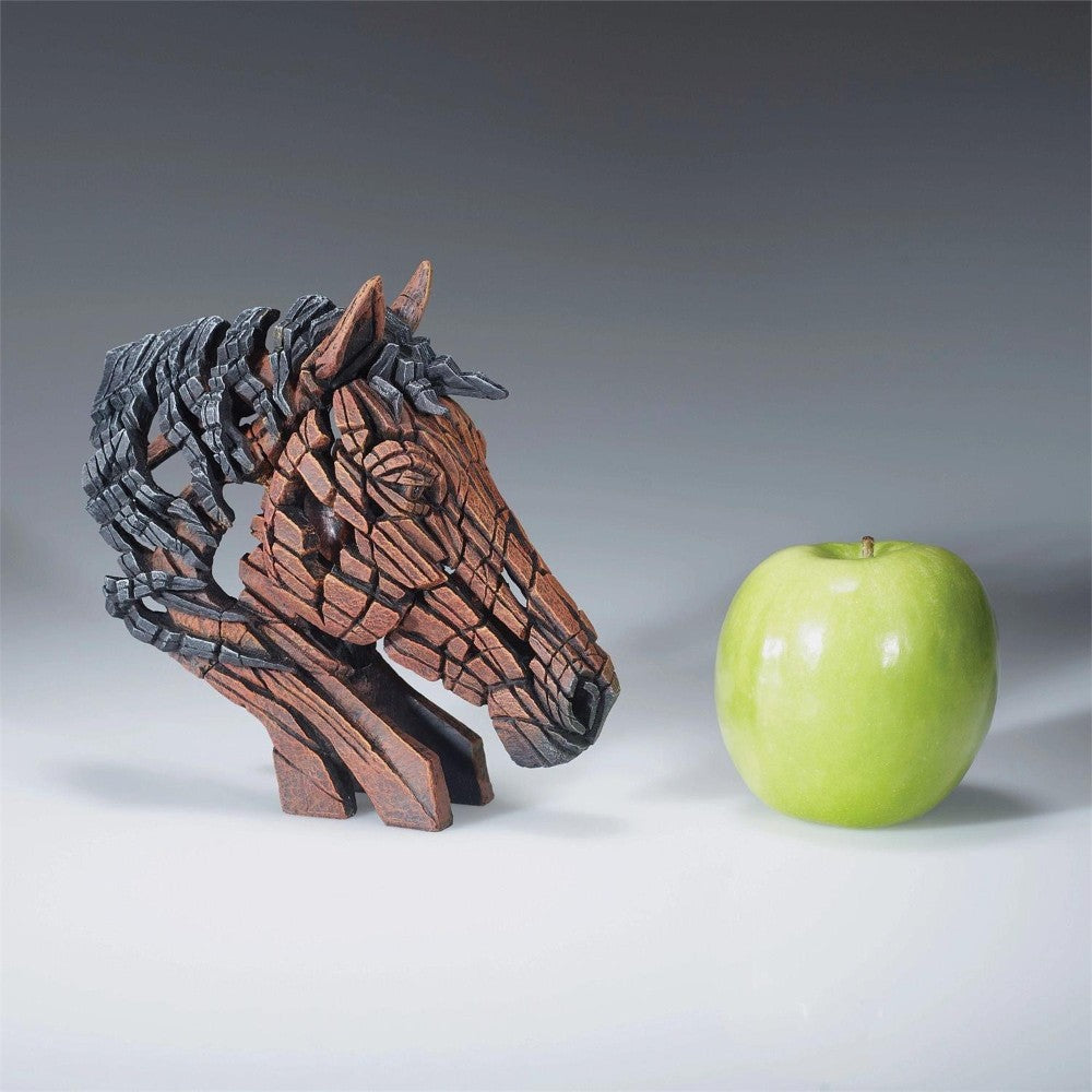 Wooden horse sculpture beside a green apple.