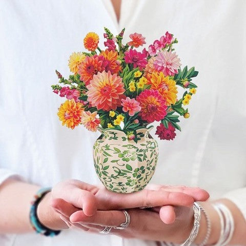 Hands holding a vase with vibrant flowers.