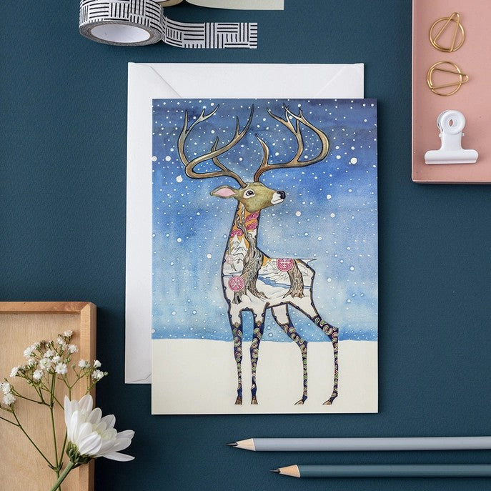 Artistic deer card with flowers surrounded by stationery on blue background.