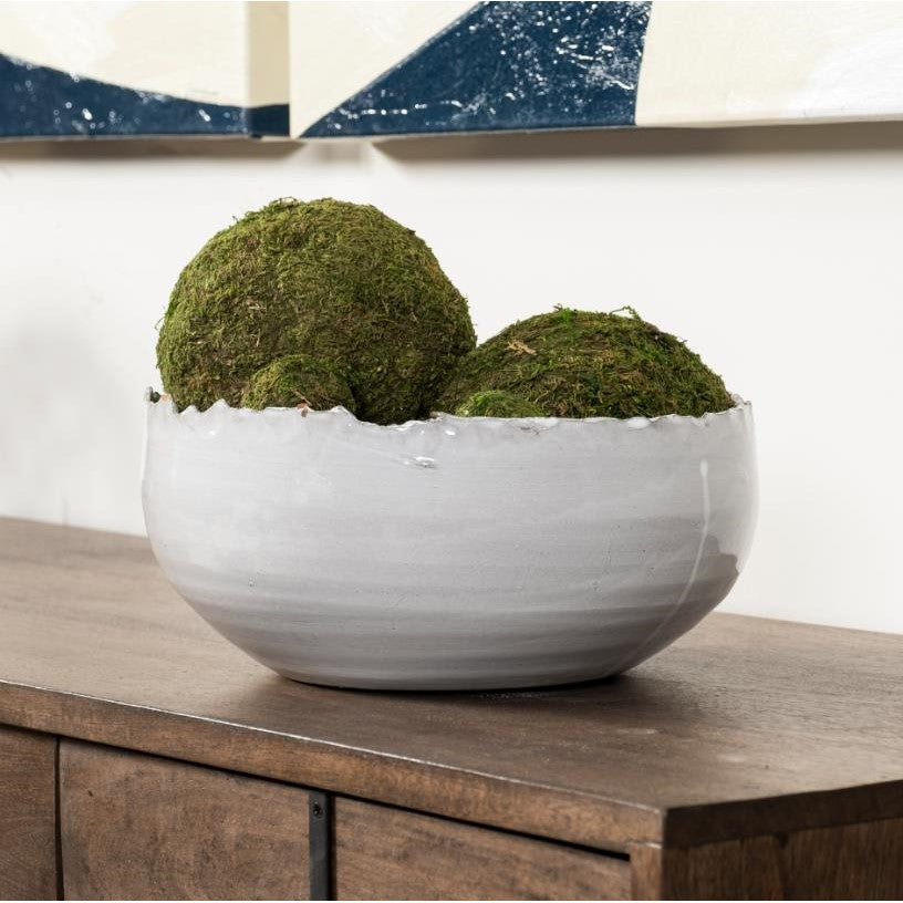 White bowl with moss balls on a wooden table.
