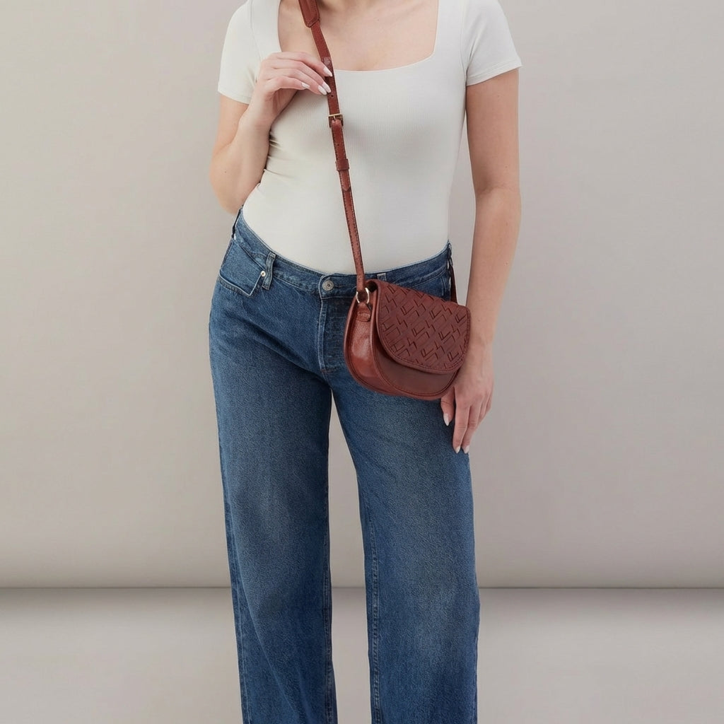 Woman in white top and jeans with a brown crossbody bag.