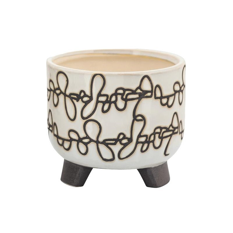 White planter with black abstract pattern on three legs.