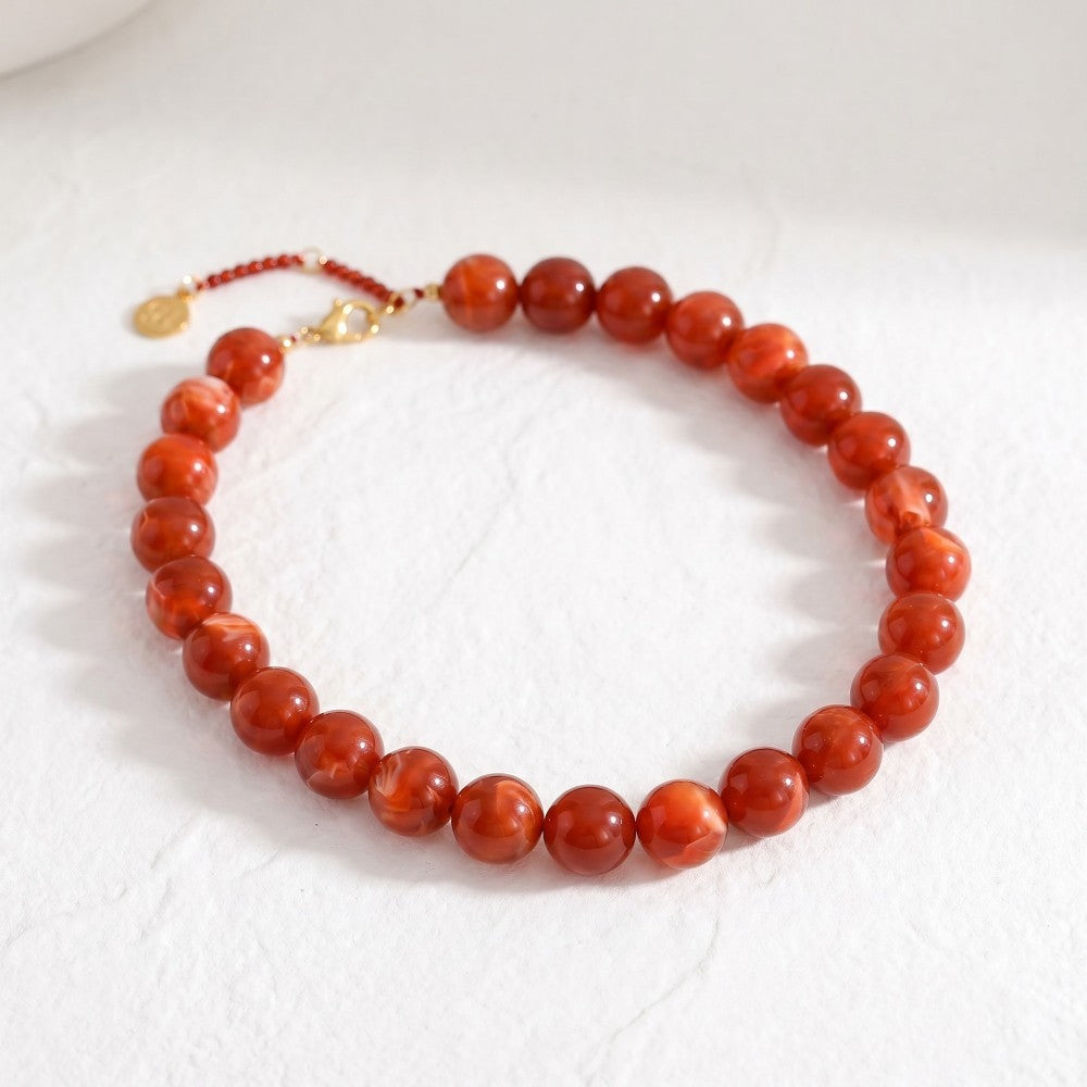 Red bead bracelet with gold clasp on a light surface.