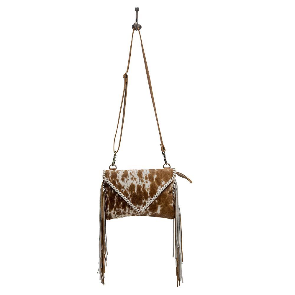 Cowhide fringe handbag with adjustable strap and woven trim.