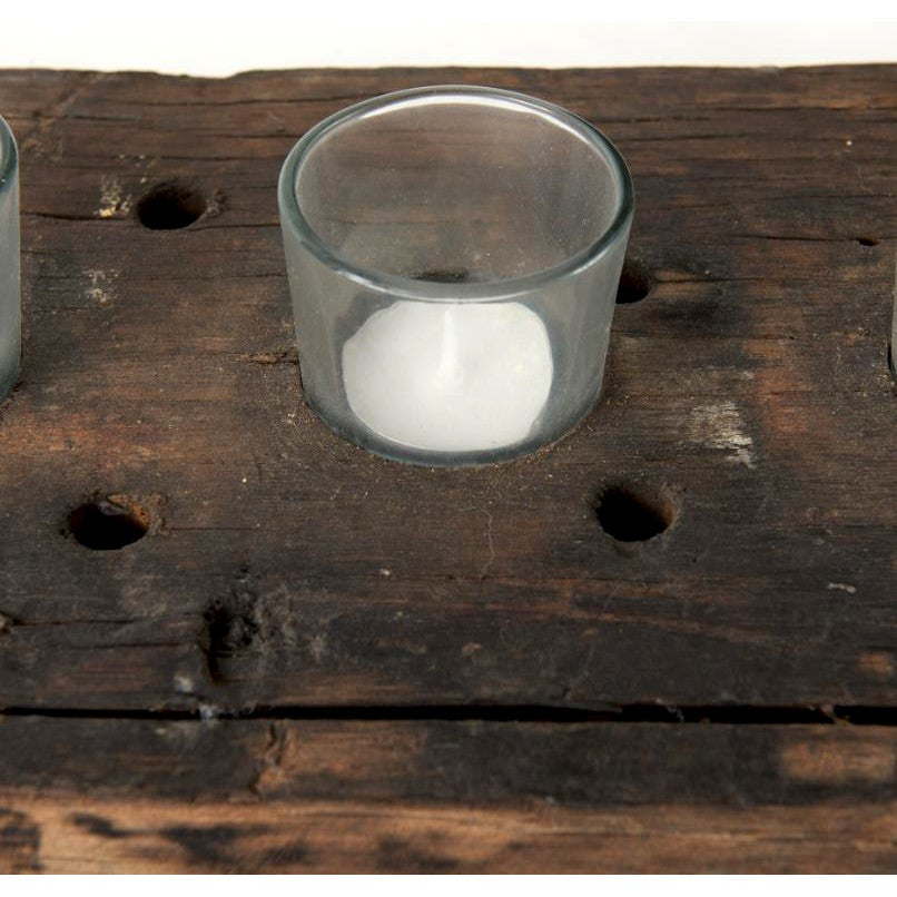 Glass candle holder on rustic wooden surface with holes.