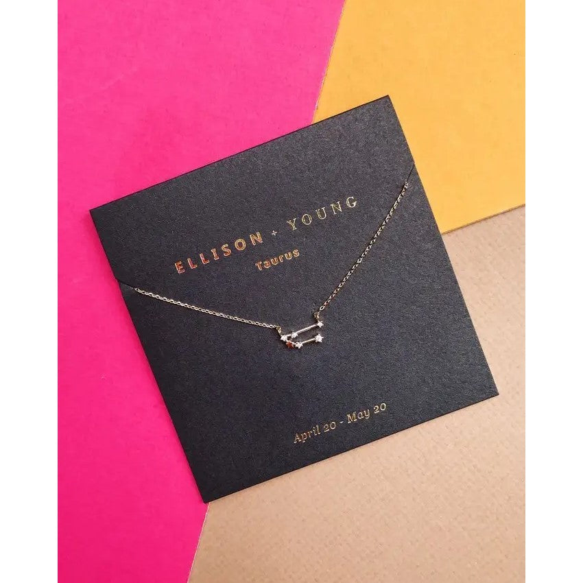 Gold necklace on a black card with pink, yellow, and beige background.