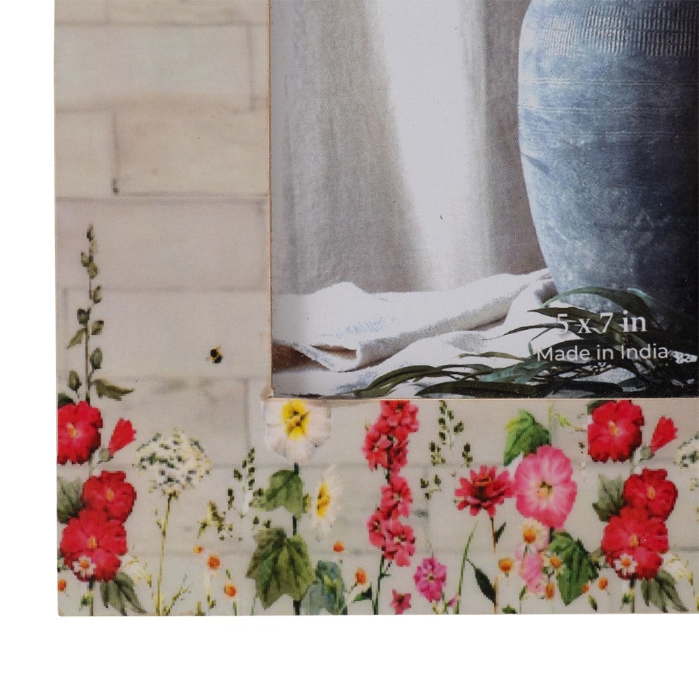 Floral-patterned frame with a blue vase and white cloth inside.