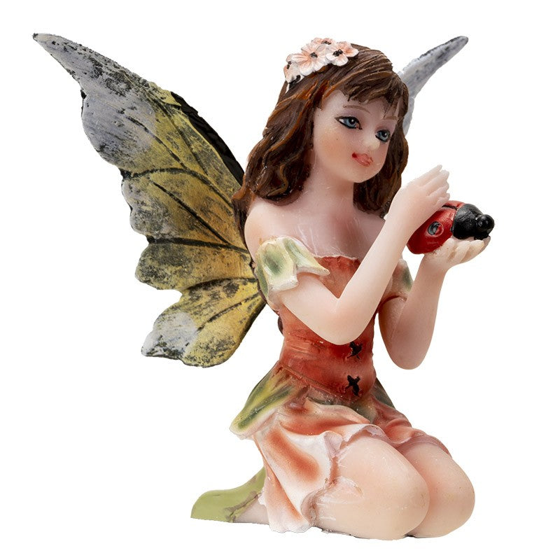 Fairy figurine kneeling, holding a ladybug, with detailed wings and floral dress.