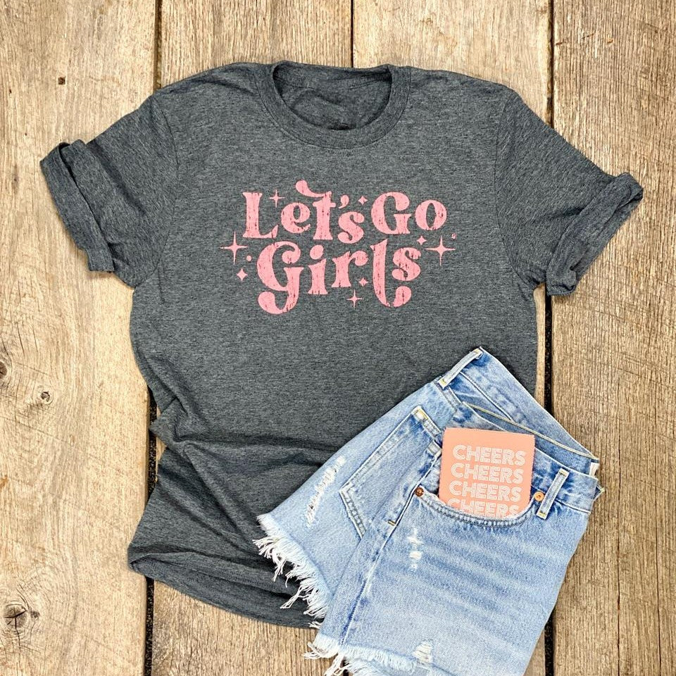 Gray tee with "Let's Go Girls" and denim shorts on a wooden surface.