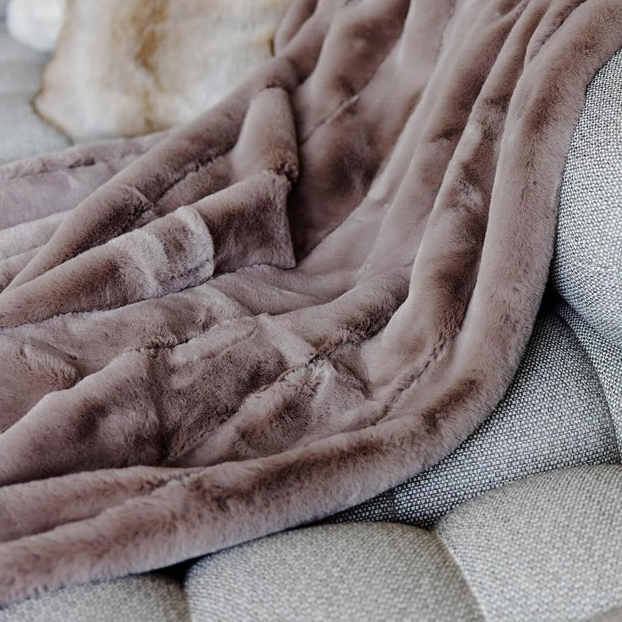 Soft, plush brown blanket draped over a textured gray sofa.