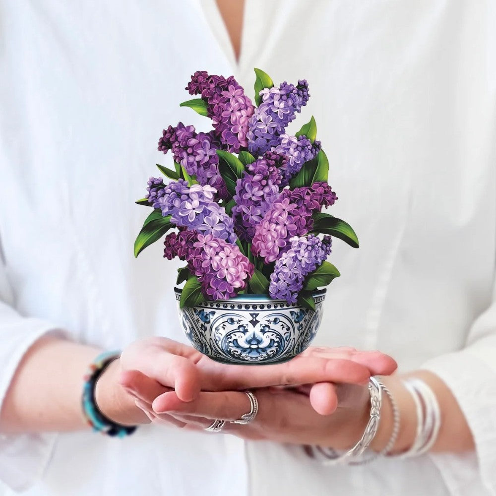 Hands holding a decorative bowl of purple and pink flowers.