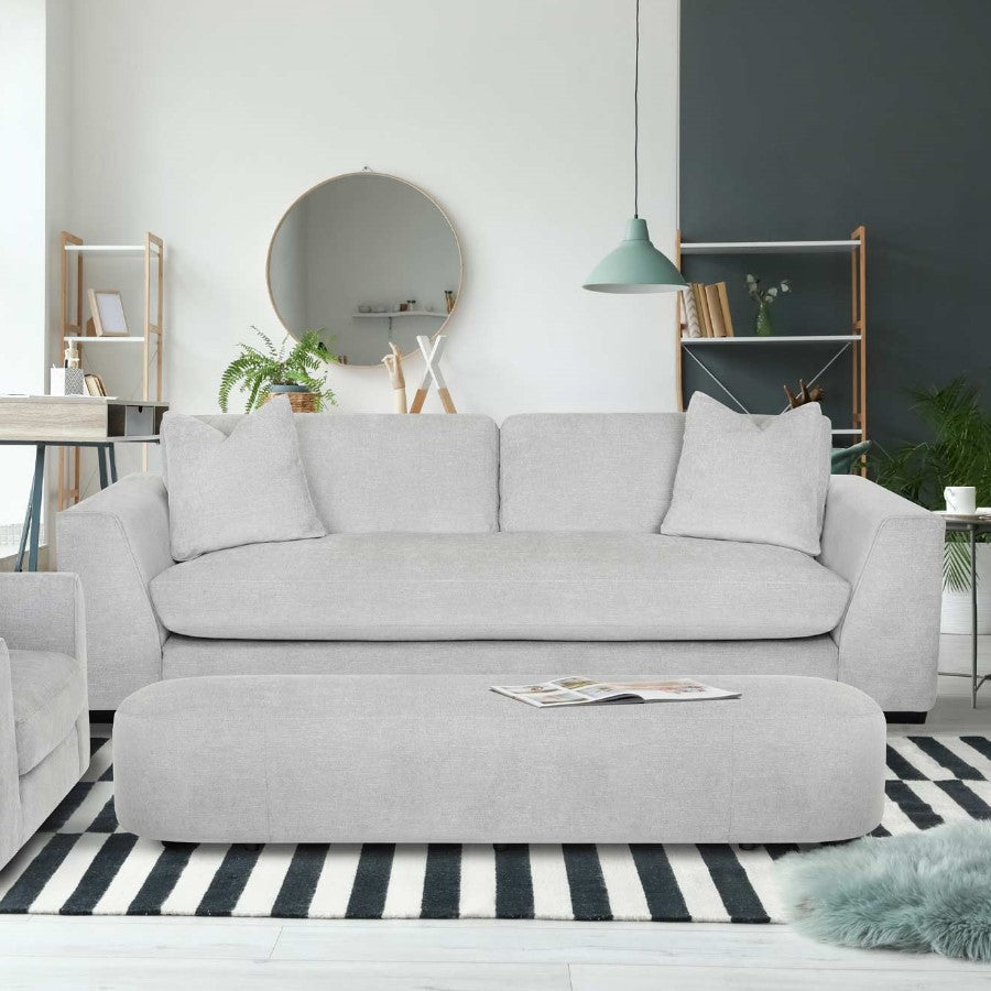 Minimalist living room with gray sofa, ottoman, and green accents.