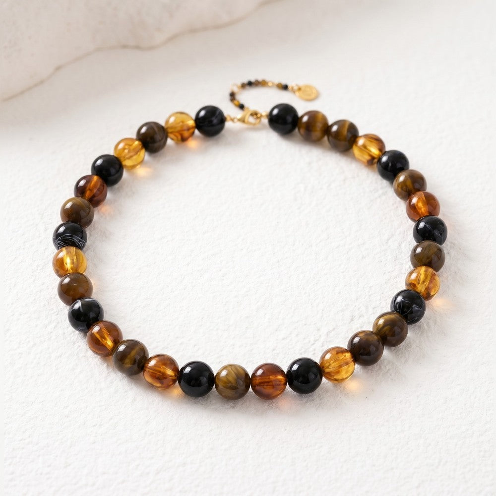 Beaded necklace with amber, brown, black tones on light textured surface.