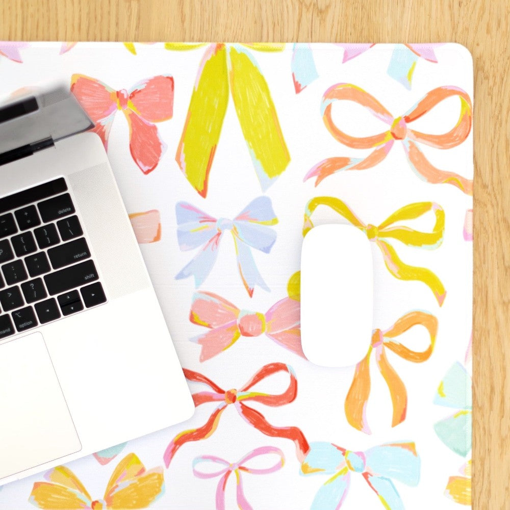 Laptop and mouse on a colorful bow-patterned desk mat.