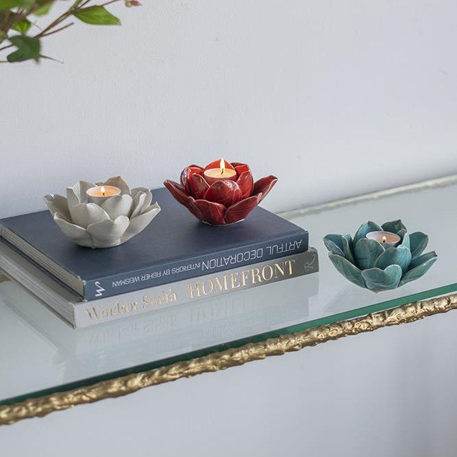 Three lotus candle holders with candles on a glass shelf.