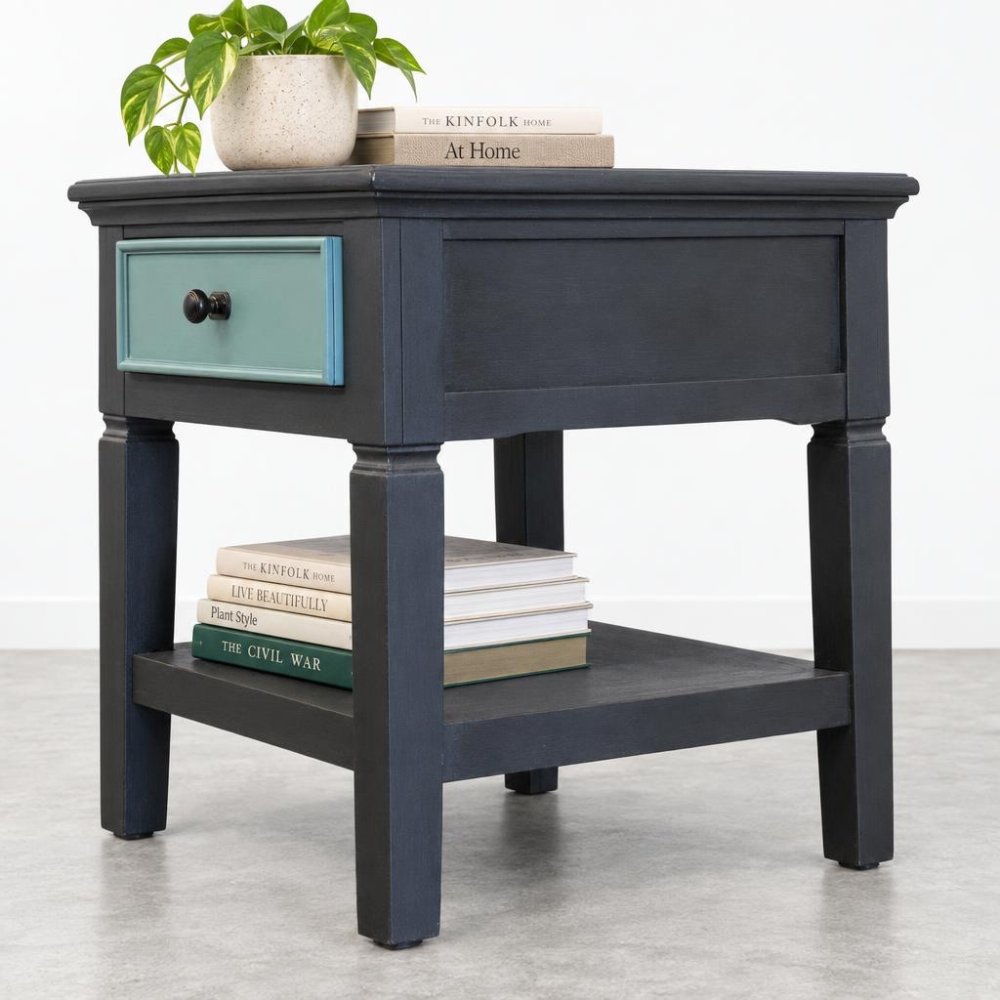 Dark end table with books, drawer, and a potted plant on top.