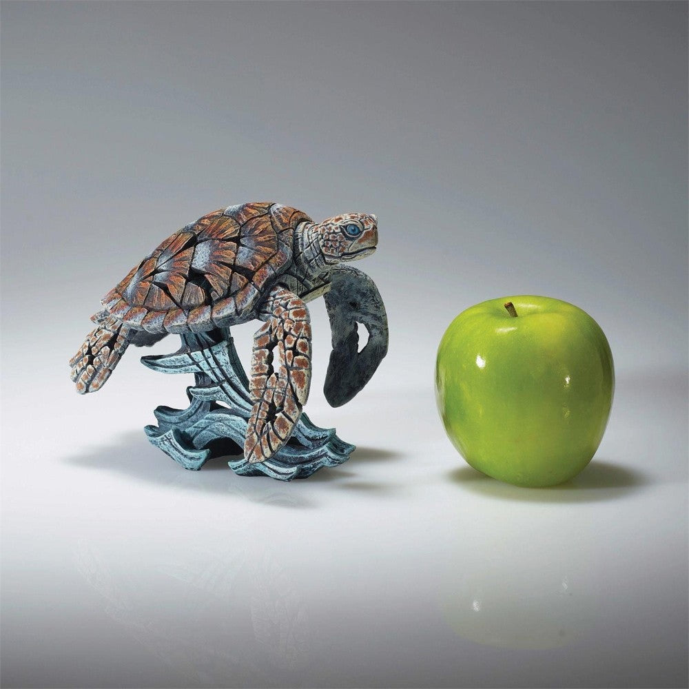 Turtle sculpture beside a green apple on a reflective surface.