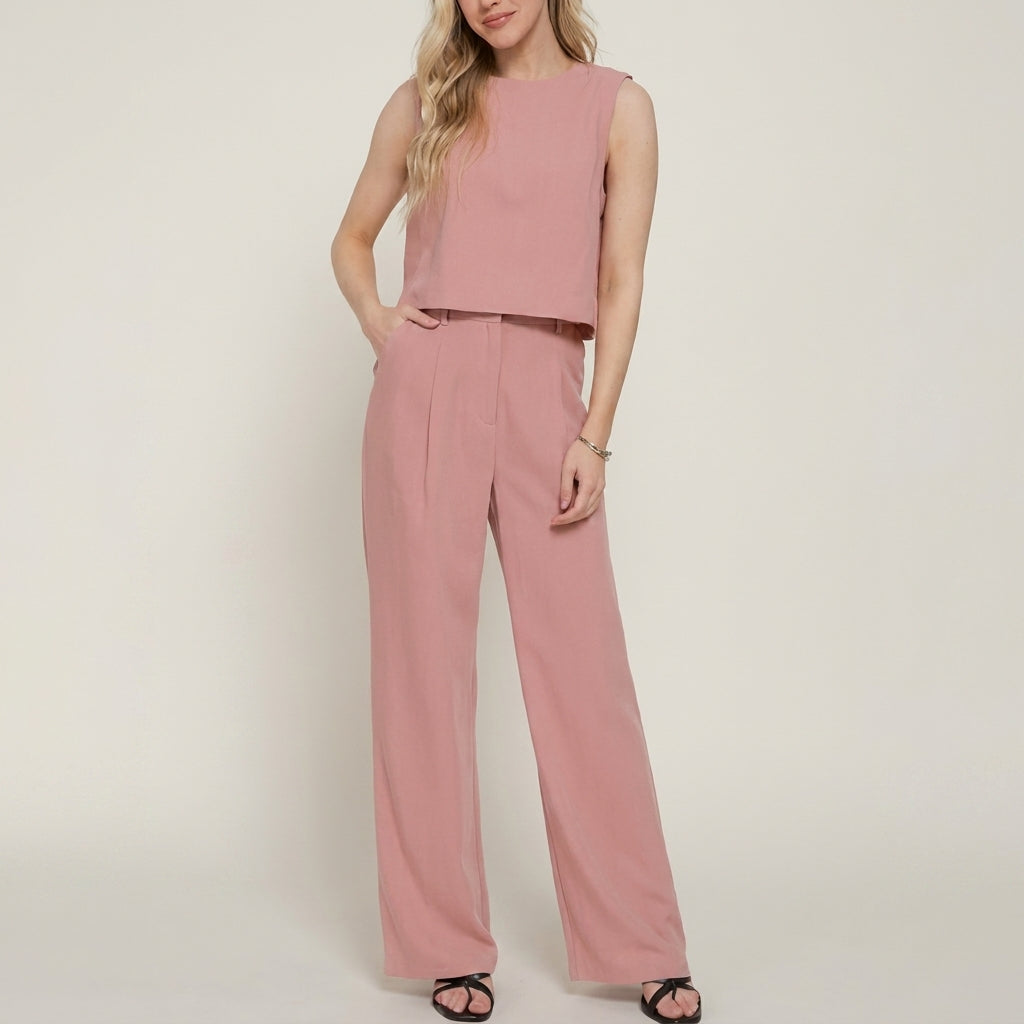 Woman in a pink sleeveless jumpsuit with light hair, standing.