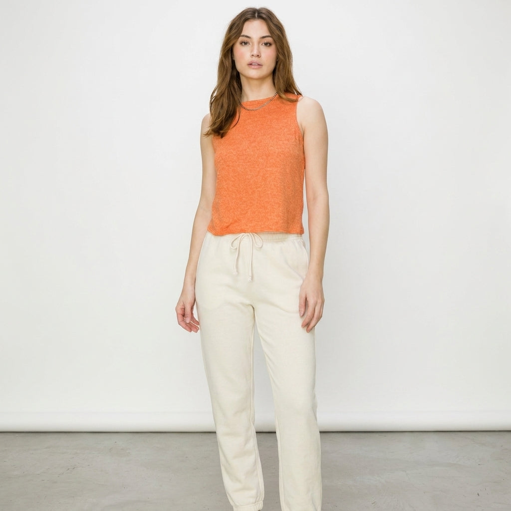 Woman in orange top and cream pants against a white background.