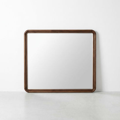 Square mirror with a dark wooden frame on a white wall.