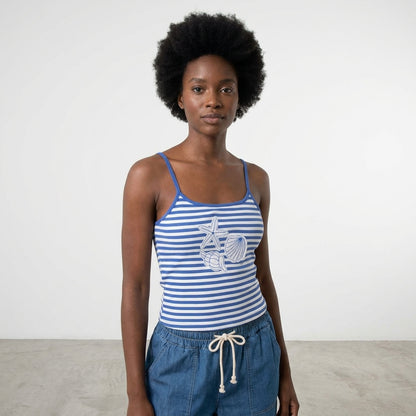 Woman in striped tank top and blue shorts, standing in a minimalist space.