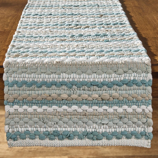 Woven table runner with blue, white, and beige stripes on a wooden table.