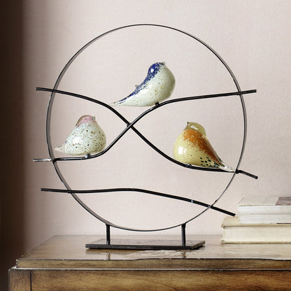 Glass birds on a metal frame sculpture, resting atop a wooden surface.