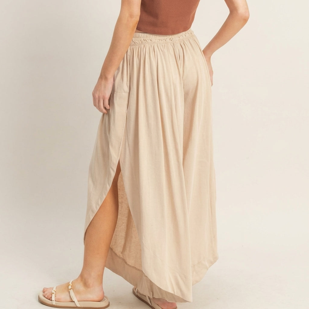 Woman in brown top with beige maxi skirt and sandals, side view.