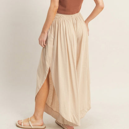 Woman in brown top with beige maxi skirt and sandals, side view.