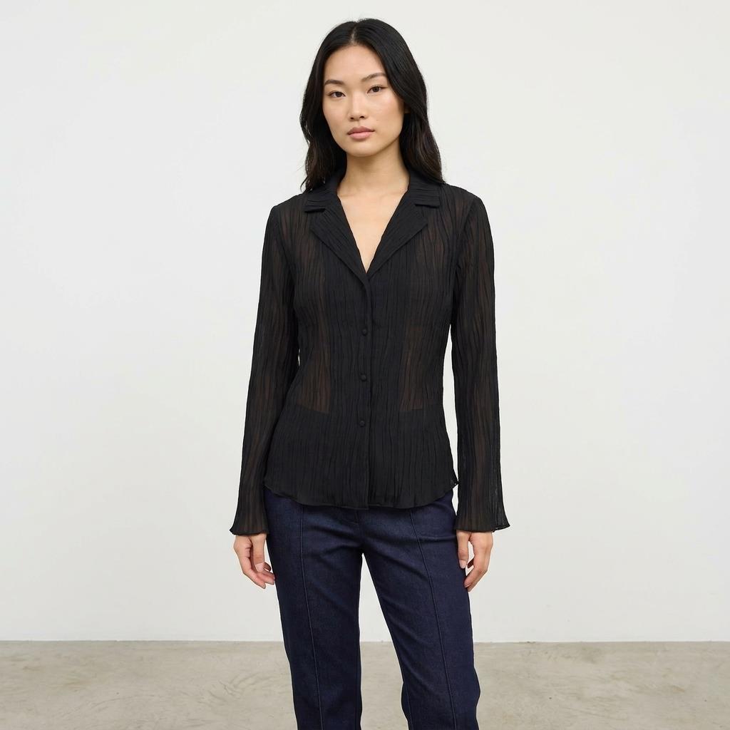 Person in a black blouse and blue jeans against a plain background.