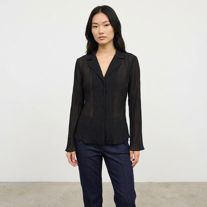 Person in a black blouse and blue jeans against a plain background.